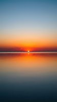 Serene sunrise over calm ocean waters with golden sun reflecting on glassy surface, transitioning from warm orange to cool blue sky, ideal for travel and nature backgrounds.