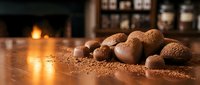 Chocolate truffles dusted with cocoa powder arranged on wooden surface with warm candlelight and blurred bottles in background, suitable for food photography and culinary content.