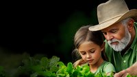 Senior Caucasian man with white beard wearing cowboy hat teaches young girl about gardening and growing vegetables in backyard garden on summer day.