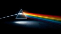 Glass prism dispersing white light into rainbow spectrum on dark surface. Physics optics demonstration showing light refraction and color separation phenomenon.