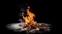 Campfire flames dancing against dark night sky with glowing embers and smoke rising from burning logs on ground creating warm outdoor atmosphere.