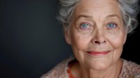 Close up portrait of senior woman with bright blue eyes and silver hair smiling warmly against dark background, showing natural aging and genuine happiness.