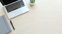 Laptop, notebook and pen arranged on light beige desk with small potted plant, overhead flat lay workspace setup for business and productivity content.