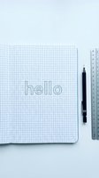 Open grid notebook with hand-lettered hello sketch, mechanical pencil and ruler on white, flat lay minimalist design concept.