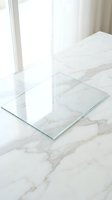 Clear glass panel on white marble surface with natural window light creating elegant minimalist interior design composition for modern home decor projects.