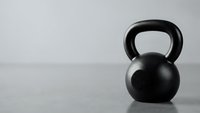 Black kettlebell on wooden floor against white wall for fitness training and strength workout exercises in minimalist gym setting.