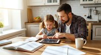 Father and daughter using digital tablet together at kitchen table for educational learning and family bonding time at home.