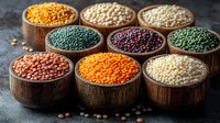 Colorful variety of raw lentils and legumes in wooden bowls on dark background. Collection of different pulses showing diverse colors and textures for cooking.