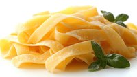 Fresh pappardelle pasta ribbons garnished with green basil leaves on white background, macro food photography showing delicate texture and curves.