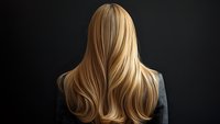 Back view of long blonde wavy hair on dark background showing professional salon styling result, highlighting natural movement and healthy shine.