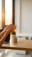 Woman hands in prayer position at wooden desk with warm sunlight streaming through window creating peaceful morning meditation atmosphere.