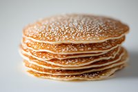Stack of fresh homemade pancakes with golden brown surface and delicate texture on light background, close up view showing layered breakfast treat.