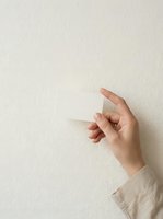Female hand holding blank transparent glass card against neutral beige wall, suitable for business card mockups, product presentations, and design templates.