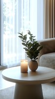 Serene home interior with glowing candle and green plant in ceramic vase on round coffee table, soft natural light through sheer curtains creates peaceful atmosphere.