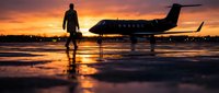 Business executive walking toward private jet at sunset with dramatic sky reflections on wet tarmac creating luxury travel atmosphere.