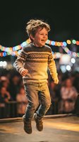 Happy young Caucasian boy with curly hair jumping and laughing outdoors at night with colorful bokeh lights in background wearing knitted sweater and jeans.