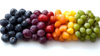 Fresh rainbow gradient made of colorful berries and grapes arranged in row on white background, healthy eating concept, natural organic fruits.