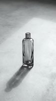 Empty glass bottle with narrow neck standing on concrete surface casting sharp shadow in natural light, suitable for cosmetics, perfume, skincare and beverage packaging mockups.