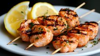 Grilled salmon skewers with fresh herbs and lemon slices on white plate, charred marks visible, garnished with chopped parsley and citrus wedges.