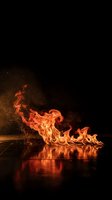 Dramatic fire flames dancing on reflective surface with sparks against black background for energy and power concepts.