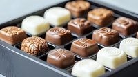 Artisanal chocolate bonbons with elegant swirl and geometric patterns in milk, dark, and white chocolate varieties arranged in luxury gift box presentation.