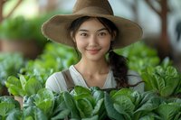 Young woman farmer wearing straw hat tending organic vegetable garden with fresh green plants, suitable for agriculture, farming, and gardening content.