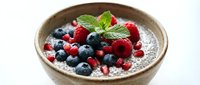 Healthy chia seed pudding topped with fresh mixed berries and mint leaves in rustic ceramic bowl for breakfast or dessert recipes.