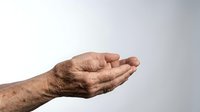 Elderly man's weathered hand with open palm in receiving gesture, showing age spots and wrinkles against neutral background for healthcare concepts.