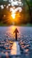 Arrow pointing upward on wet asphalt surface against golden sunset light creating bokeh effect and reflections, symbolizing growth, success and aspirational concepts.