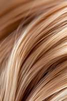 Smooth flowing blonde hair strands in macro photography showing detailed texture and natural highlights, suitable for beauty and haircare advertising.