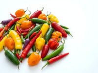Colorful assortment of fresh hot chili peppers in red, yellow, orange and green varieties scattered on white background for culinary and cooking projects.
