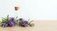 Essential oil bottle with cork stopper surrounded by fresh lavender flowers on wooden surface against neutral background for aromatherapy and wellness.