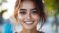 Young Asian woman with radiant smile and natural makeup against blurred green background, casual updo hairstyle showing genuine happiness and confidence.