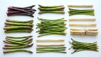 Assorted fresh asparagus varieties including green, purple, and white spears arranged in organized bundles on white background for culinary and food styling use.