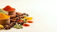 Colorful spices and herbs in wooden bowls with cinnamon sticks, star anise, and cardamom pods scattered on light background for culinary cooking.