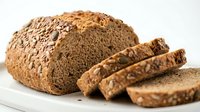 Freshly baked whole grain bread loaf with mixed seeds and nuts, sliced on white plate. Healthy artisan bakery product for breakfast and meals.