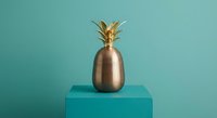Golden metallic pineapple decoration on turquoise cube against teal background for modern interior design and luxury home decor concepts.