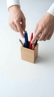 Hands selecting pen from wooden desk organizer with colorful writing tools for office workspace organization and productivity.