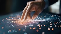 Female hand touching glowing digital surface with orange light particles and bokeh effects, representing technology interaction and future interface concept.