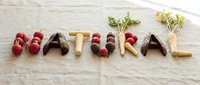 Word NATURAL spelled with fresh vegetables and root crops on linen fabric background, promoting healthy organic food concept.