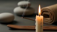Zen spa composition with burning candle, smooth stones, wooden bowl and towel creating peaceful meditation atmosphere for wellness and relaxation.