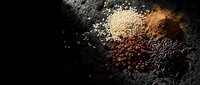 Assorted grains and legumes scattered on dark textured surface creating rustic food ingredient display for cooking and nutrition concepts.