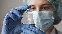Female healthcare worker in protective mask and gloves holding medical vial for vaccination, pharmaceutical research and clinical treatment applications.