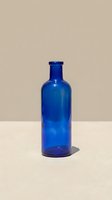 Empty cobalt glass bottle with cork-style cap isolated on neutral beige background, suitable for beverage packaging, apothecary, vintage design, and product mockup applications.