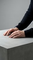 Close-up of hands in black knitted sweater resting on white surface, minimalist composition with soft lighting for modern lifestyle concepts.