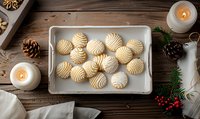 Homemade butter cookies with swirled pattern on baking tray, surrounded by pine cones, lit candles and holiday decorations on rustic wooden table. Festive baking scene.