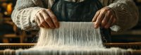 Artisan weaver working at traditional wooden loom, close-up view of hands manipulating white threads. Authentic handcraft process showcases textile making heritage.