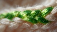 Vibrant green and white braided threads in macro photography showing intricate weaving pattern and textile texture detail with soft selective focus effect.