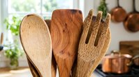Wooden kitchen utensils including spoon, spatula and fork arranged in rustic cooking space with copper pots and natural lighting for culinary design.