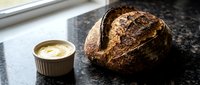 Freshly baked artisan sourdough bread loaf with crispy crust next to creamy butter on dark countertop for bakery, food, and culinary design projects.